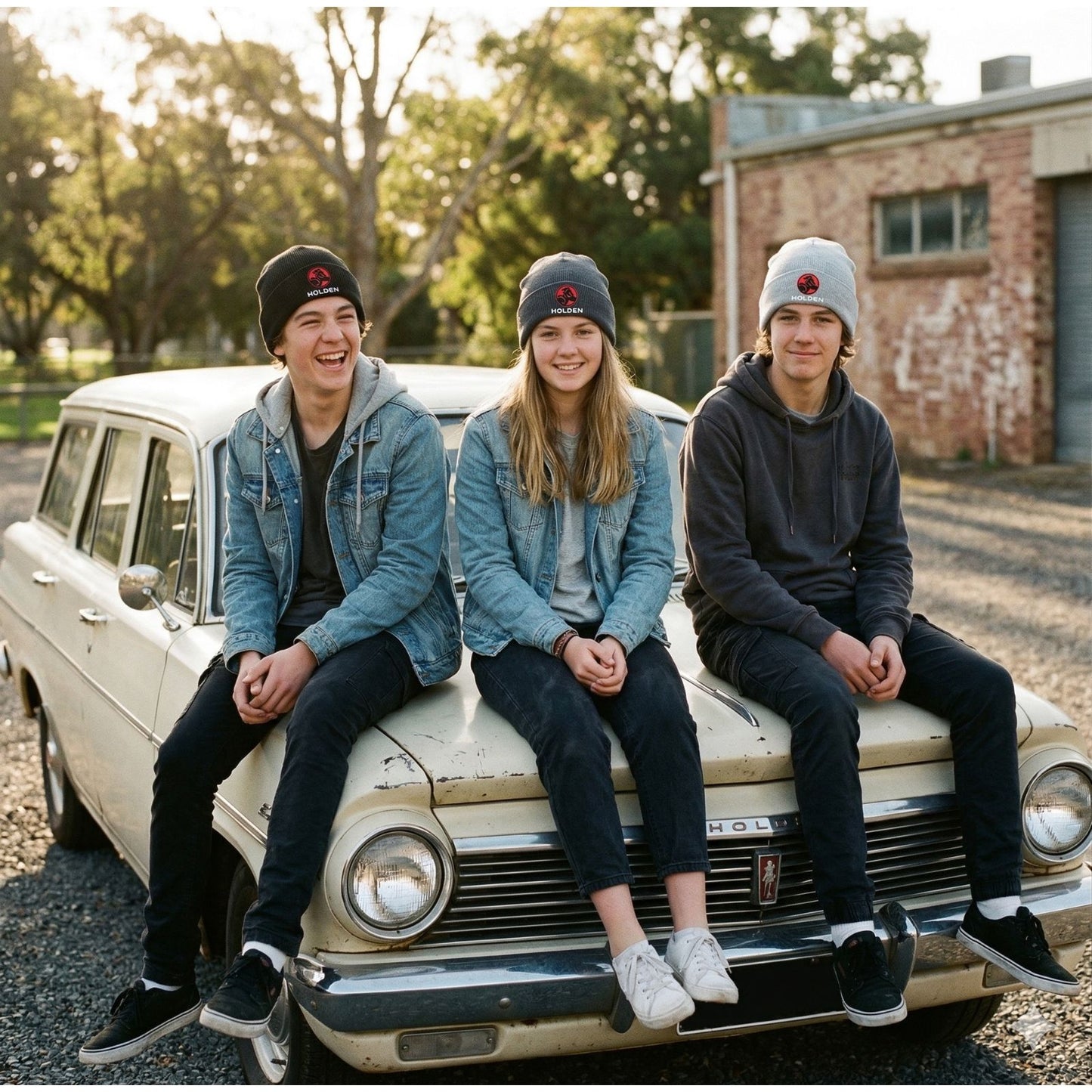 Three young people sitting on an old Eh Holden car in a rural setting